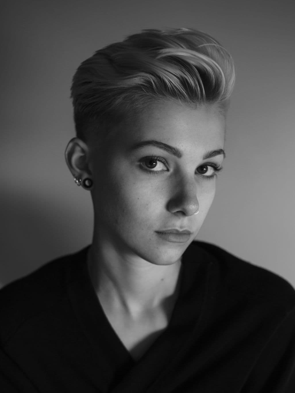 A simple, black and white photo of Emerson, a white person of Eastern European descent, with short blonde hair, in a black sweater.