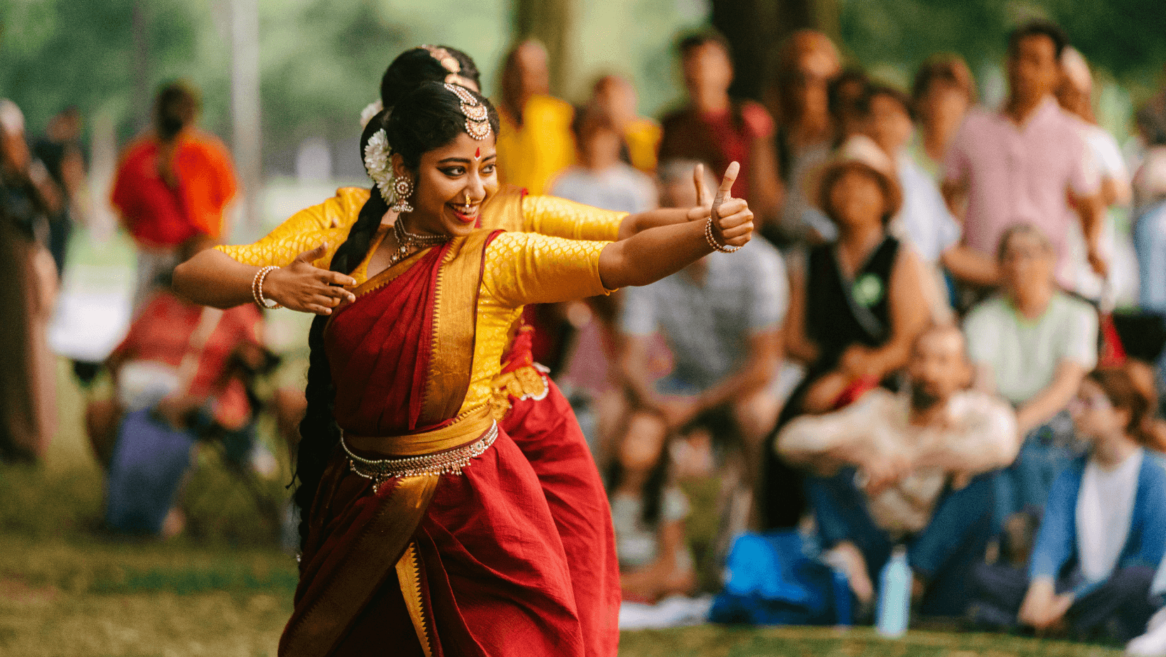 Dancers in yellow tops with red saris and gold jewelry performing outdoors in front of a crowd