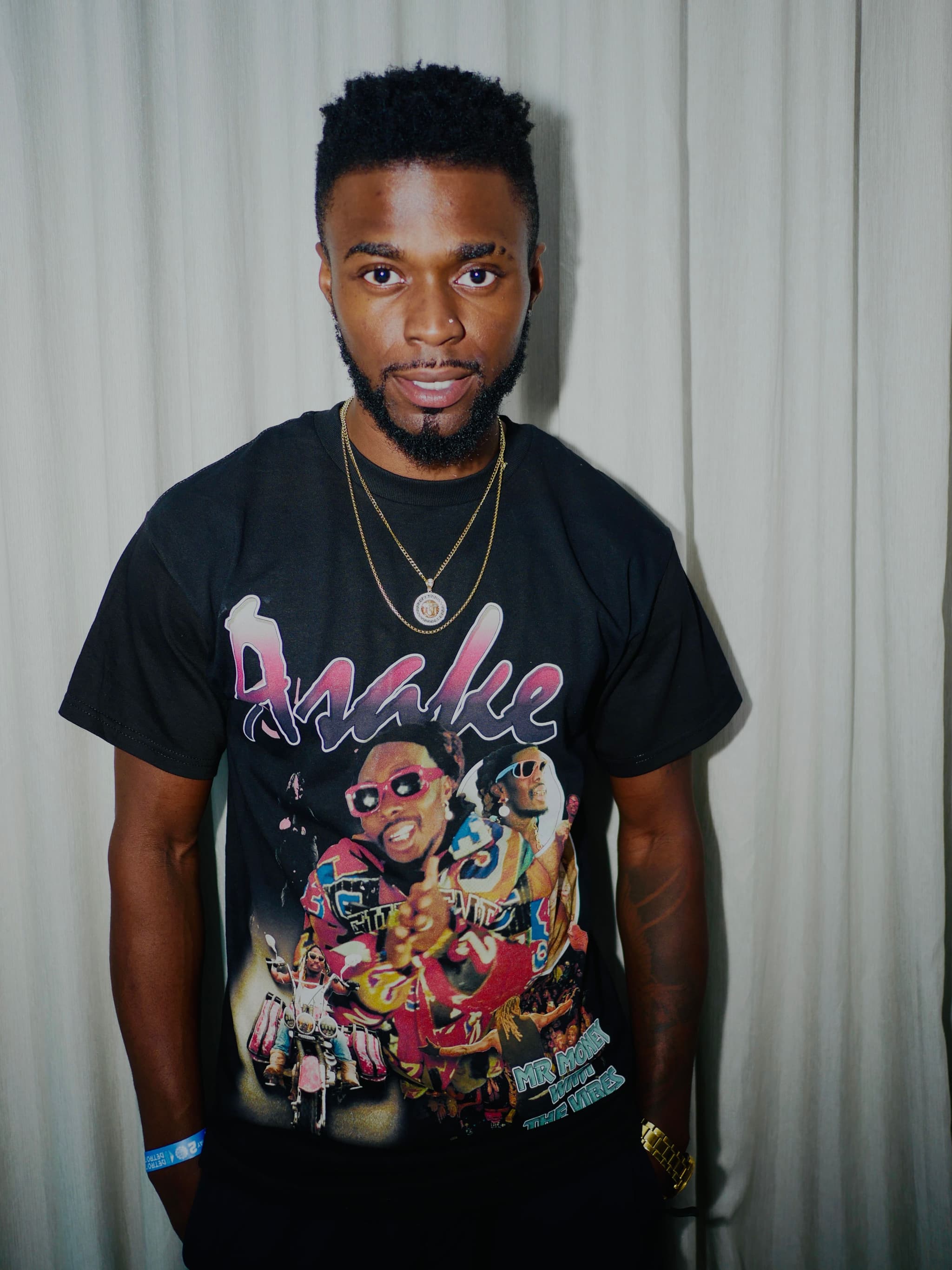 Martin, a Black woman with short curly black hair soflty smiling, in front of charcoal white backdrop, wearing a black graphic t shirt and and two necklaces..